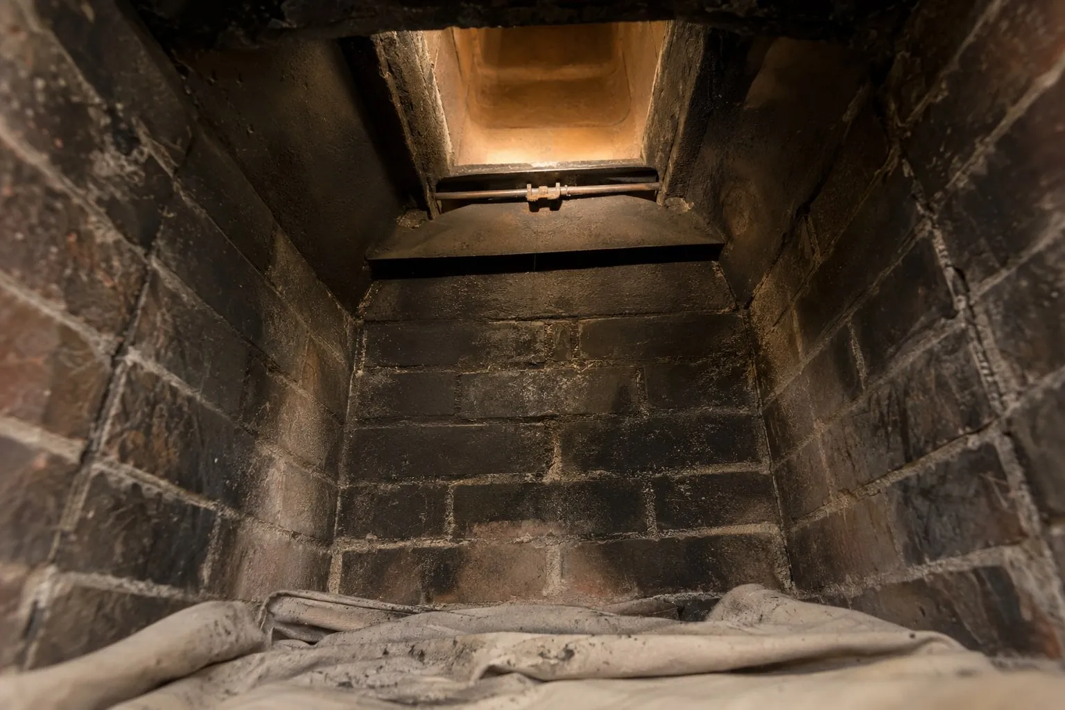 Looking up inside a brick fireplace at the damper and the flue, lit from below, with a dust sheet on the floor